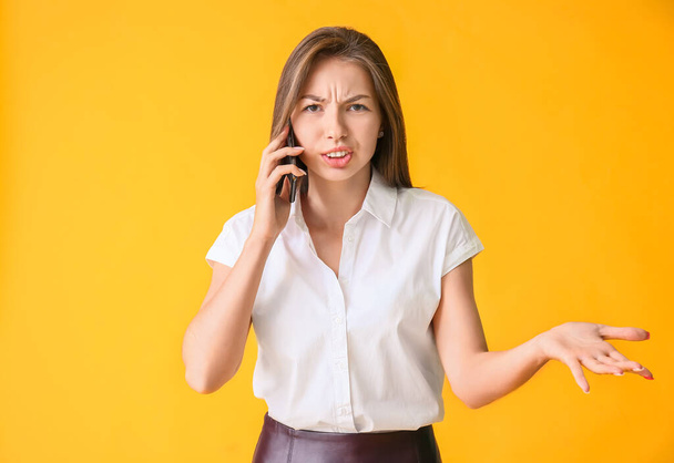 Недовольная молодая деловая женщина разговаривает по мобильному телефону на цветном фоне - Фото, изображение