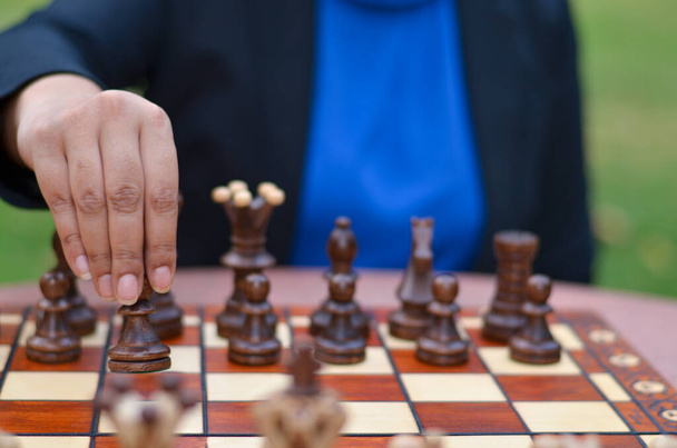チェスをしている女の子が黒い駒を手に取った駒でチェスボードの上を進んでいる。概念-アイデア、戦略 - 写真・画像