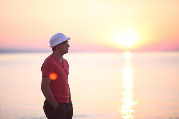 View of a man with a summer hat admiring the sunrise on the beach, beautiful background of the sun and sea - Foto, Imagem