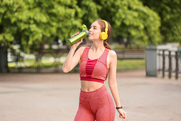 Sporty young woman with headphones and water outdoors - Photo, Image