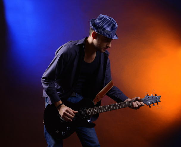 Young musician playing guitar on dark color background - Fotoğraf, Görsel