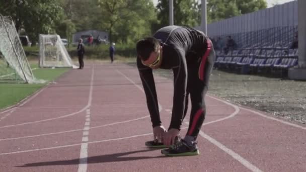 2 de marzo de 2019. Ucrania, Kiev. Tema deporte y salud. Hombre caucásico joven hace ejercicio de calentamiento estiramiento de los músculos antes de entrenar en correr en un estadio de la ciudad cinta de correr - Metraje, vídeo