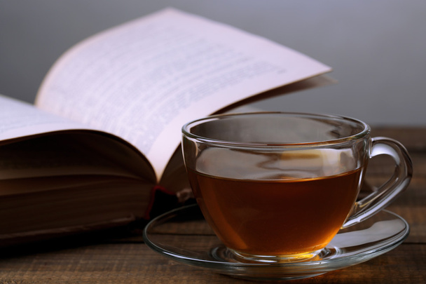 Taza de té caliente con libro sobre mesa sobre fondo gris
 - Foto, imagen