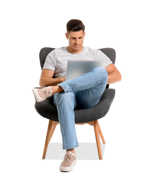 Молодой человек с ноутбуком расслабляется в кресле на белом фоне - Фото, изображение