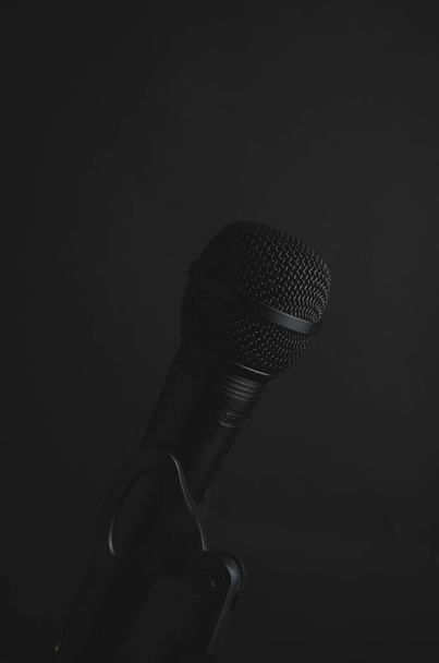 A vertical closeup shot of a black microphone on a black background - Foto, imagen