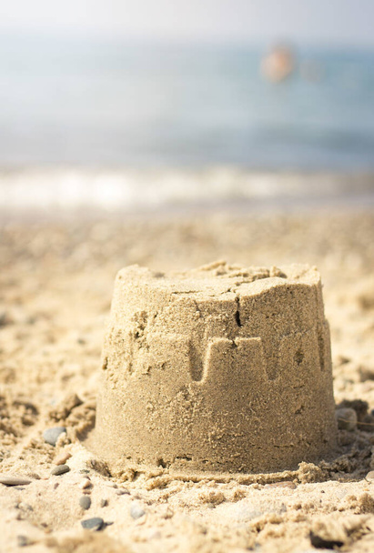 Um tiro vertical de um pequeno castelo de areia na praia sob a luz do sol com um fundo embaçado
 - Foto, Imagem