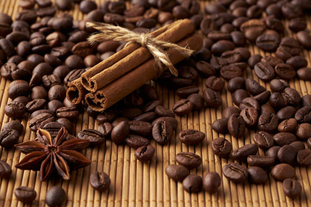 Roasted brown whole coffee beans, tied sticks of cinnamon and anise on a bamboo mat - Valokuva, kuva