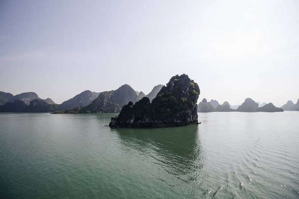 The limestone islands topped by trees and their reflection on the turquoise water of Ha Long Bay in Vietnam - Fotografie, Obrázek