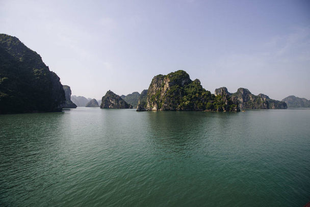 De kalkstenen eilanden bekroond met bomen en hun reflectie op het turquoise water van Ha Long Bay in Vietnam - Foto, afbeelding