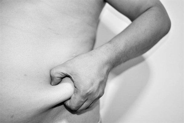 Fotografia in bianco e nero su sfondo bianco primo piano mano di un uomo cattura pancia sullo stomaco per mostrare l'obesità e il grasso in eccesso. - Foto, immagini