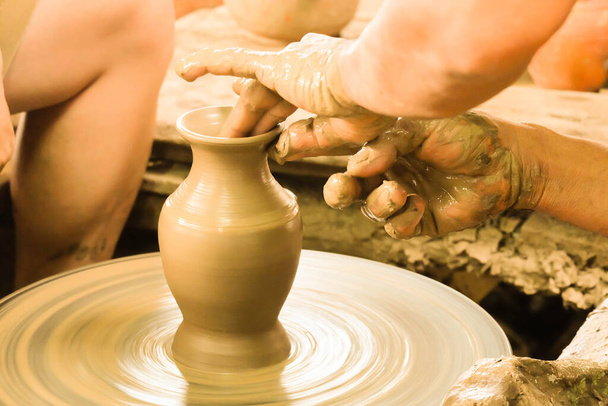 Крупным планом руки глиняного гончара делают вазу на вращающемся столе, используя свои руки и пальцы, чтобы тщательно украсить и умело сделать работу красивой. - Фото, изображение