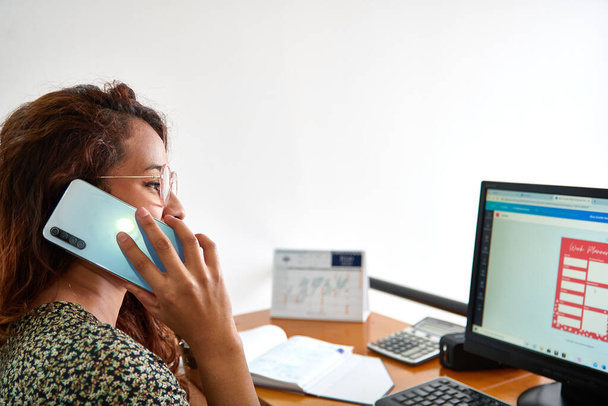 fiatal nő beszél telefonon előtt laptop az irodában - Fotó, kép