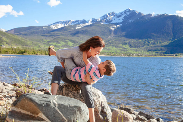 Jeune mère touristique embrassant son fils près du lac avec une belle vue sur les montagnes sur le fond. Les femmes voyagent en Amérique avec leur famille. Concept de famille heureuse - Photo, image