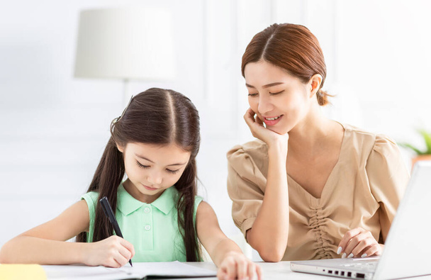 Mother is working and teaching her daughter doing home work - Фото, зображення