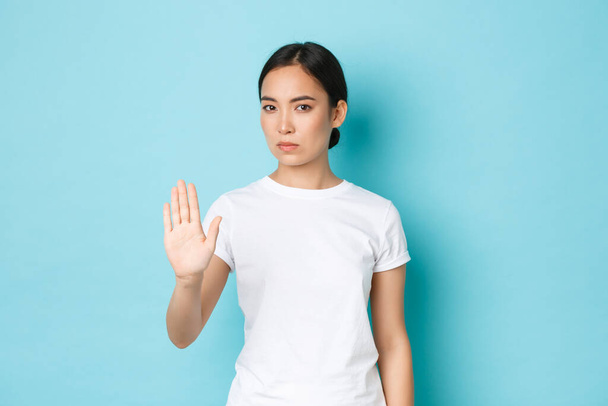 Sério confiante asiático mulher parar algo ruim, levantando a mão em proibição, discordar ou proibir gesto, de pé fundo azul e recusar má oferta, rejeitando
 - Foto, Imagem