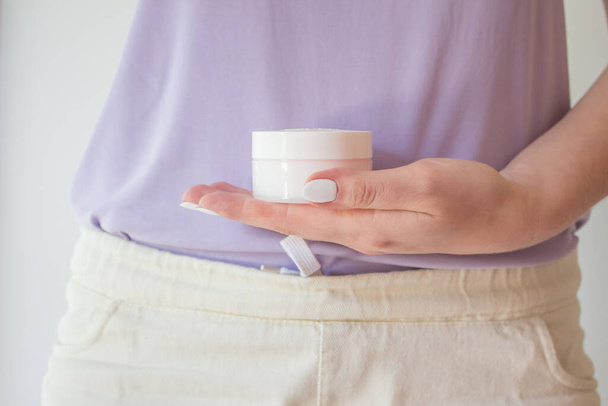  A jar of anti-aging cream is held in the hands of a woman with a beautiful manicure. Natural organic eco-friendly cosmetics for skin rejuvenation. - Photo, Image