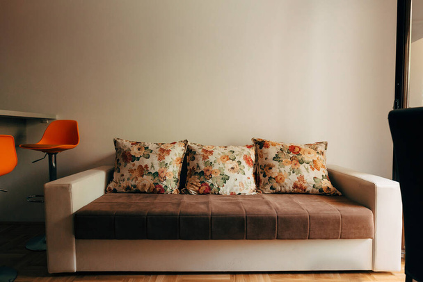 Egy puha, konvertibilis kanapé három párnával egy narancssárga bárszékkel és világos szürke háttérrel.. - Fotó, kép