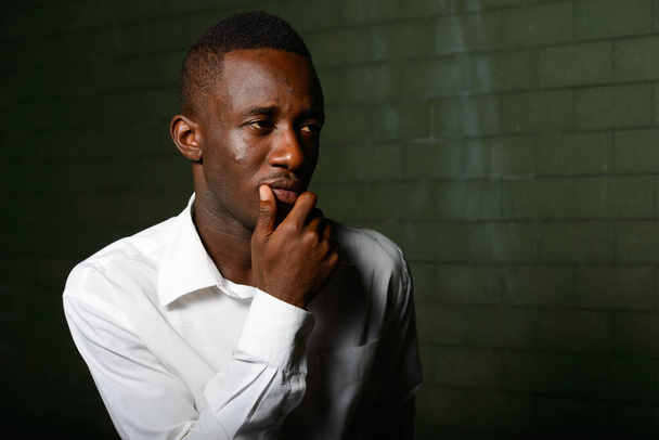Portrét mladého afrického obchodníka ve tmě proti cihlové zdi v noci - Fotografie, Obrázek