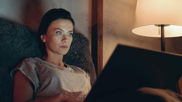 Woman browsing internet on notebook. Female reelancer typing on laptop at night. - Photo, Image