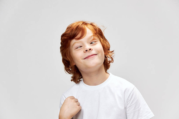 Ritratto di bambino dai capelli rossi smorfia t-shirt bianca divertente studio - Foto, immagini