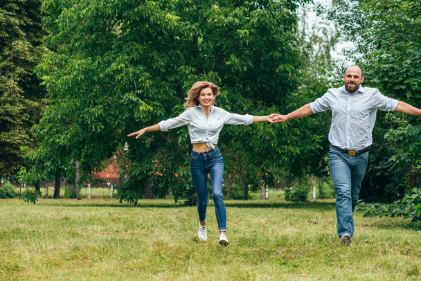 Gay man and woman in jeans run to meet camera on green grass lawn  - Foto, afbeelding
