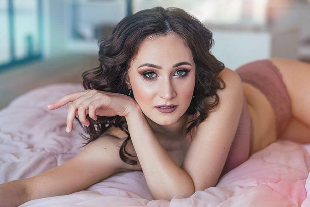 portrait de jeune femme avec maquillage et coiffure boucles en sous-vêtements sur le lit  - Photo, image
