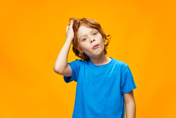 Мальчик рыжие волосы голубая футболка желтый изолированный фон веснушки и удивленный взгляд ослепленный взгляд - Фото, изображение