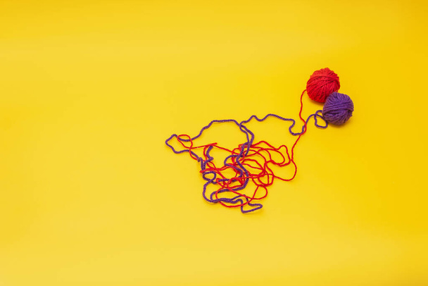 a tangles of red and blue woolen threads lies unraveled on a yellow background. the view from the top - Фото, зображення