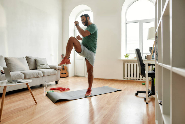 Get Fit. Full length shot of young active man watching online video training on laptop, exercising during morning workout at home. Sport, healthy lifestyle - 写真・画像