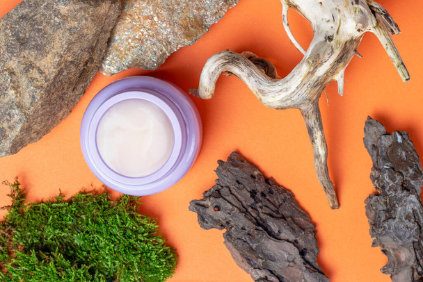 A jar of cream stands near stones and dried branches on a orange background, view from above - Photo, Image