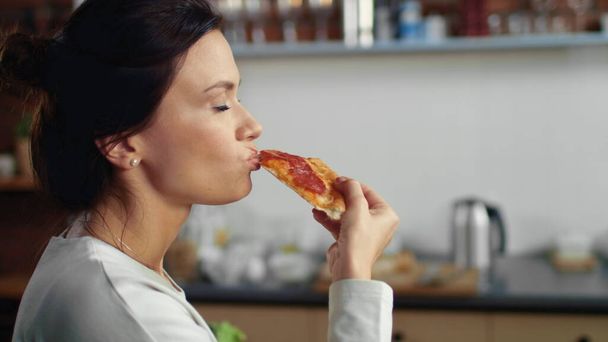 Жінка кусає шматочок піци вдома. Голодна дівчина їсть піцу з коробки
. - Фото, зображення
