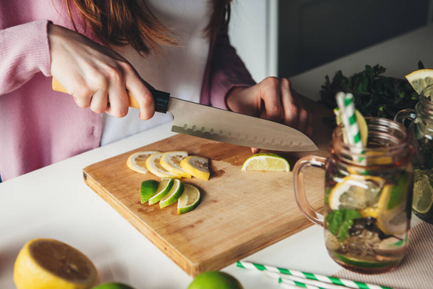Foto vista lateral de uma senhora de gengibre preparando mojito em casa cortando limão com uma faca
 - Foto, Imagem