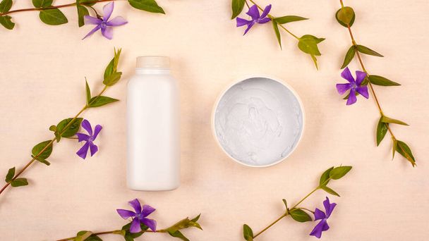 frascos blancos con cosméticos sobre un fondo beige con flores silvestres violetas vista superior plana laico. cuidado de la piel, belleza, limpieza de la piel - Foto, Imagen