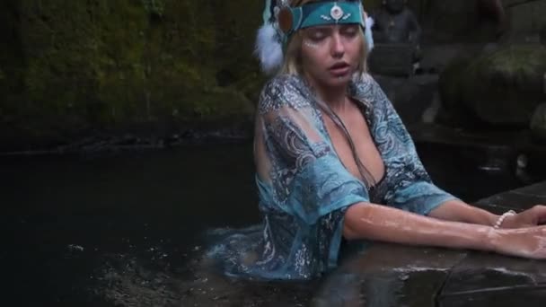 Salaperäinen nuori nainen eksoottisissa vaatteissa uimassa järvessä luolan pyhäkössä - Materiaali, video
