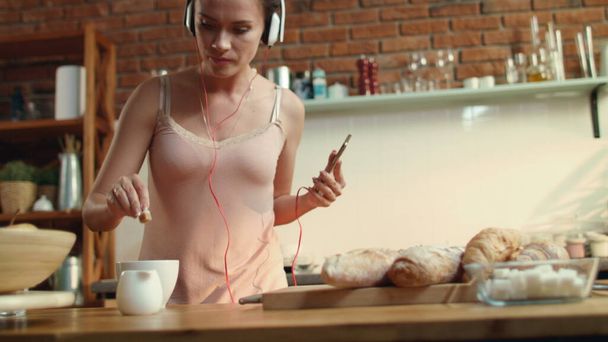 Mujer joven mojando azúcar en el café. Bailarina escuchando música en la cocina. - Foto, Imagen