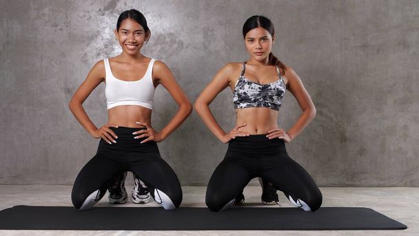 Дві вродливі азійські жінки займаються спортом на йога маті в спортзалі. Щасливі подружки проводять свій вільний час у спортивному центрі. - Фото, зображення