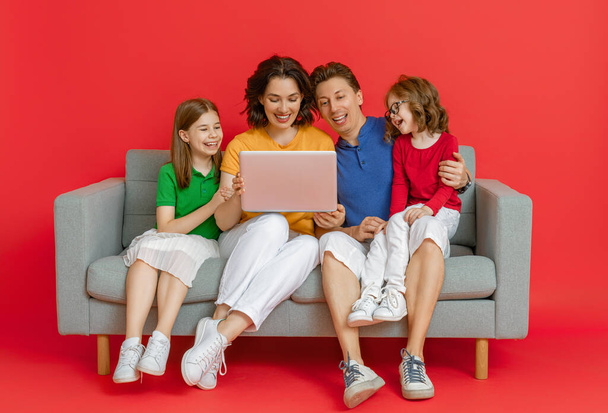 Šťastná milující rodina na jasném pozadí barev. Otec, matka a dcery dívky používají notebook pro vzdálenou konverzaci s přáteli. Tati, máma a krásný děti se baví doma.. - Fotografie, Obrázek