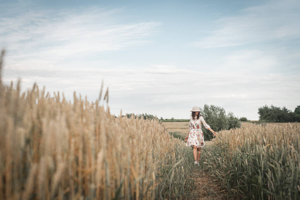 Beautiful young brunette girl in a wheat field walking on the trail - Valokuva, kuva