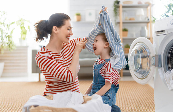 Beautiful young woman and child girl little helper are having fun and smiling while doing laundry at home. - Fotoğraf, Görsel