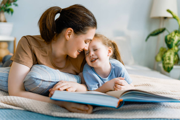 Happy loving family. Pretty young mother reading a book to her daughter on the bed at home. - Zdjęcie, obraz