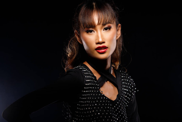 Portrait of 20s Asian Woman tanned skin brown blonde hair style Cosmetic Make up, black dress red lips. Girl poses over dark Background isolated - Fotografie, Obrázek