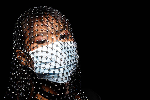 Foto de la cara Retrato de los años 20 Mujer asiática bronceado maquillaje cosmético. Chica decorar diamante Crystal Net cabeza de la cubierta y usar máscara protectora sobre fondo oscuro aislado, mirada de cerca Moda - Foto, Imagen