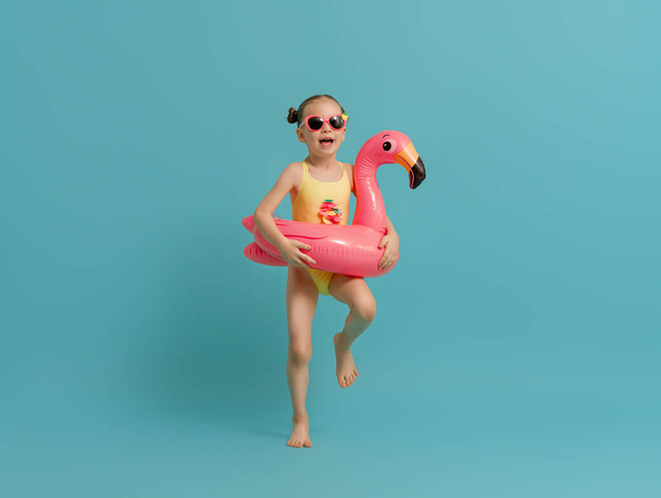 Happy child wearing swimsuit. Girl with swimming ring flamingo. Kid on a colored turquoise background. - Foto, immagini