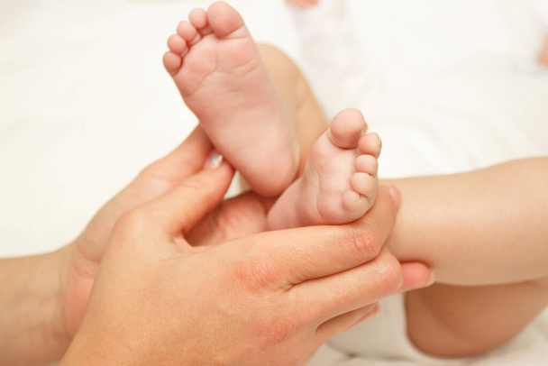 Hands of woman holds baby foot, soft focus background - Foto, imagen