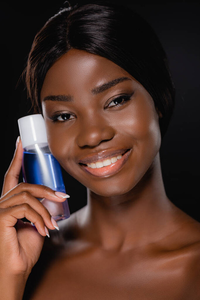 portrait of african american naked woman holding micellar water isolated on black - Photo, Image