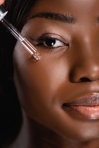 close up view of african american woman applying serum on face isolated on black - Valokuva, kuva
