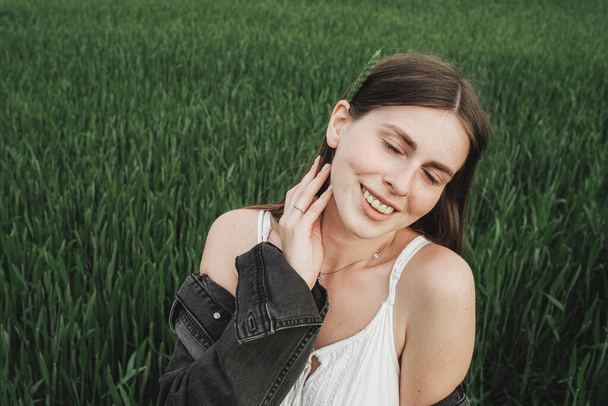 Young Stylish Girl in White Dress and Denim Jacket Spends Time in Green Wheat Field - Foto, Imagem