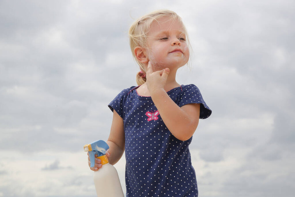 Милая маленькая девочка с кремом для защиты от загара на пляже. Лосьон для защиты ребенка от солнца во время летних каникул. Уход за кожей детей во время путешествия. - Фото, изображение