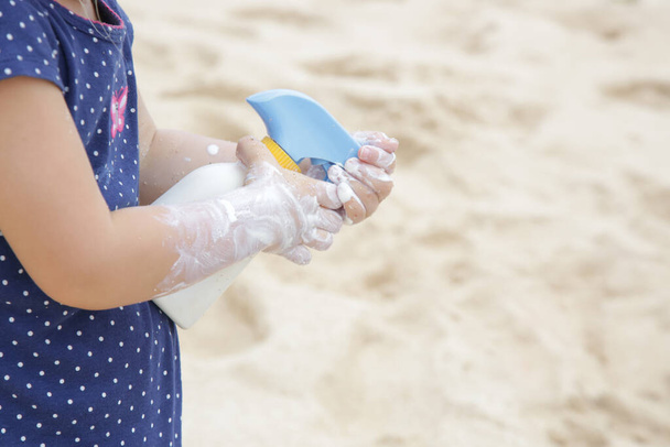 Çocuk ellerinin plajda güneş kremi sürerken görüntüsünü kapat. Yaz tatilinde bebeği güneşten korumak için güneş kremi. Yolculuk sırasında çocuk sağlığı ve cilt bakımı. - Fotoğraf, Görsel