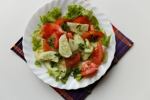 Comida vegana, ensalada de primavera con tomates, pepinos, perejil y eneldo en una mesa blanca - Foto, Imagen